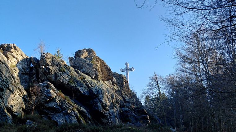 A beautiful rock with a cross, surrounded by trees and clear sky. The path leads through nature.