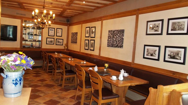 Een gezellig restaurant met houten tafels en stoelen. Aan de muren hangen verschillende schilderijen, en op de tafels staan bloemen en servies.