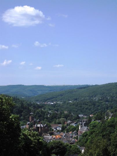 Eine malerische Aussicht auf ein Dorf in einem bewaldeten Tal. Im Hintergrund sind sanfte Hügel unter einem klaren blauen Himmel sichtbar.