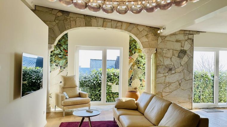 A modern living space with a comfortable sofa and a small table. Large windows offer a view of a green landscape.