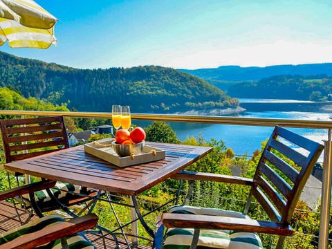 Een mooi uitzicht op een meer met groene heuvels. Een tafel met twee glazen en een fruitmand staat op het terras.