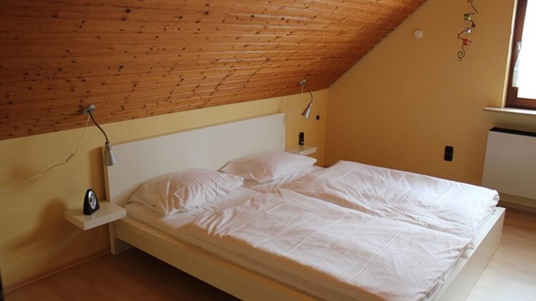 A cozy bedroom with a double bed and simple nightstands. The walls are painted in soft colors and the ceiling has a wooden covering.