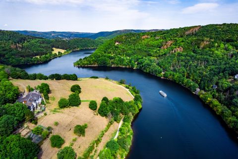 A picturesque landscape with a river, surrounded by green hills and forests. A small boat is gently gliding on the water.