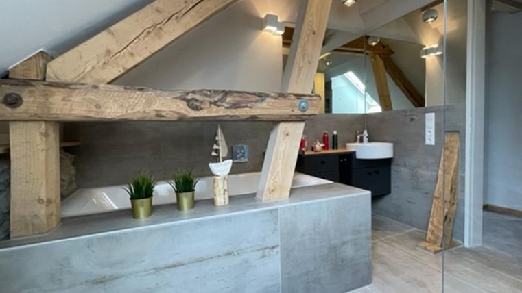 Een moderne badkamer met een vrijstaand bad en houten details. De wanden zijn in neutrale kleuren en er komt veel daglicht binnen.