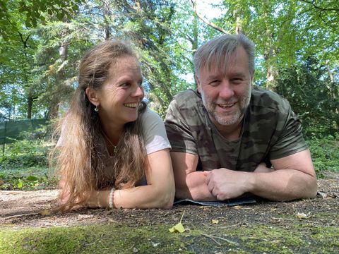 Ein Paar liegt im Grünen und lächelt miteinander. Umgeben von Bäumen und Natur strahlen sie Freude und Entspannung aus.