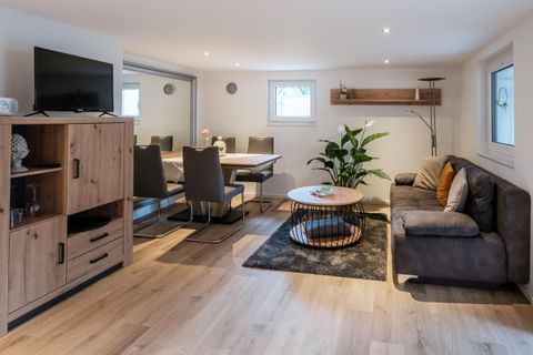 Ein modernes Wohnzimmer mit einem gemütlichen Sofa und einem niedrigen Tisch. Der Raum ist hell und einladend, mit Pflanzen und einem Fernseher.