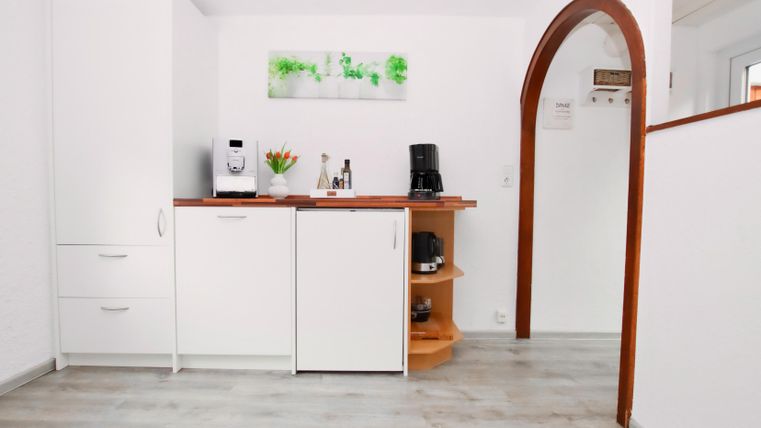 Een moderne keuken met witte kasten en een houten planken. Op het aanrecht staan een koffiezetapparaat en een vaas met bloemen.