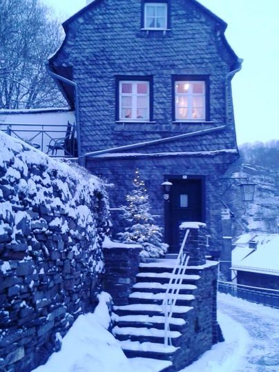 A charming stone house in a snowy landscape. In front of the entrance door stands a small Christmas tree.