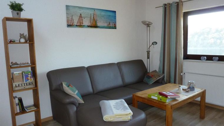 A cozy living room with a gray sofa and a wooden table. A picture of sailboats hangs on the wall.
