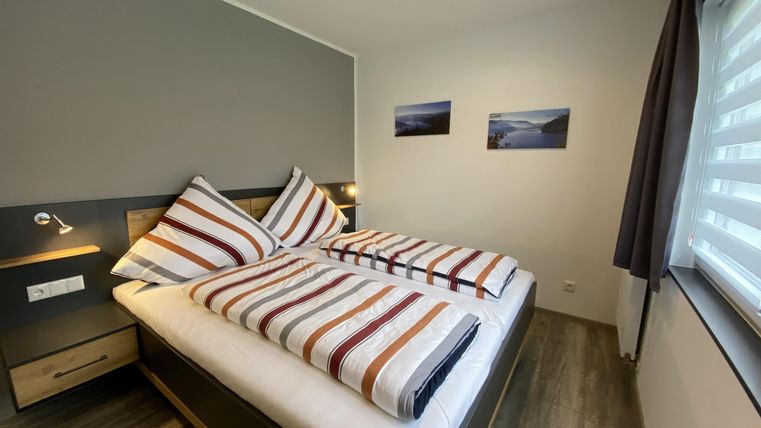 Een moderne slaapkamer met twee eenpersoonsbedden en gestreepte dekbedden. De muren zijn in neutrale kleuren gehouden, en er zijn twee schilderijen en een raam met gordijnen.