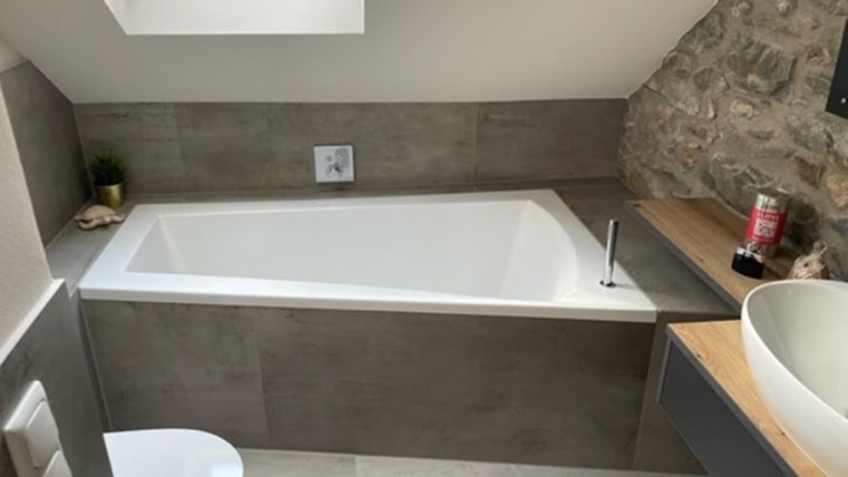 Een moderne badkamer met een witte badkuip en een wastafel. De muren zijn gedeeltelijk gedecoreerd met steenbekleding.
