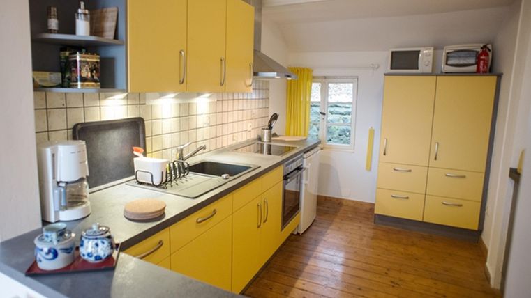 A bright kitchen with yellow cabinets and wooden floor. The amenities include a sink, a stove, and a coffee machine.