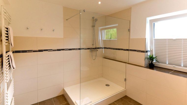 A modern bathroom with a transparent shower and bright tiles. Naturalistic decorations such as plants and windows ensure brightness.