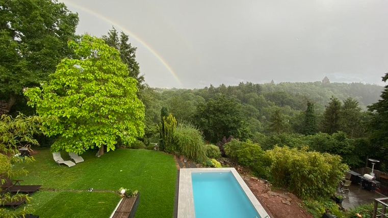 Een grote tuin met een zwembad en een regenboog op de achtergrond. De omgeving is groen en bosrijk.