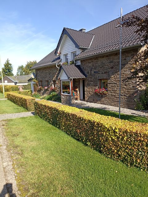 Ein charmantes Haus aus Naturstein mit einem gepflegten Garten und einer lebhaften Hecke. Die Fassade ist mit Blumen dekoriert, was einladend wirkt.