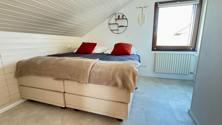 Een gezellige slaapkamer met een tweepersoonsbed en twee rode kussens. Grote ramen zorgen voor veel natuurlijk licht.
