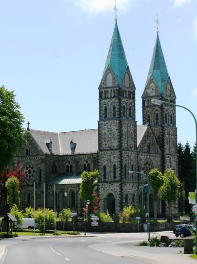An impressive church with two towers and green roofs. Surrounded by trees and a quiet street.