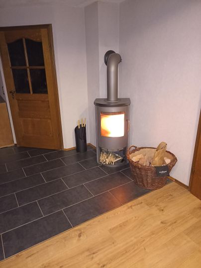 Ein moderner Kamin mit flammen im Wohnzimmer. Neben dem Kamin steht ein Korb mit Holz.