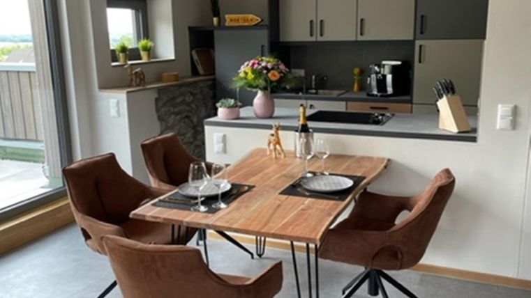 Een gezellige eetruimte met een houten tafel en moderne stoelen. De keuken op de achtergrond is goed uitgerust en helder verlicht.