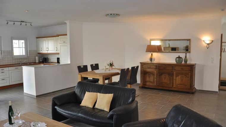 Ein helles, modernes Wohnzimmer mit einer offenen Küche und einem Essbereich. Die Einrichtung ist schlicht und einladend, mit einem schwarzen Sofa und einem Holztisch.