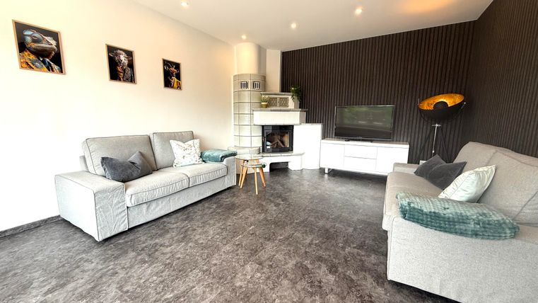 Een moderne woonkamer met twee lichte banken en een televisie. De muren zijn deels donker afgewerkt en met afbeeldingen versierd.