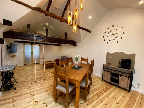 Een lichte woonkamer met houten vloeren en zichtbare balken. Een grote eettafel en moderne verlichting creëren een uitnodigende sfeer.