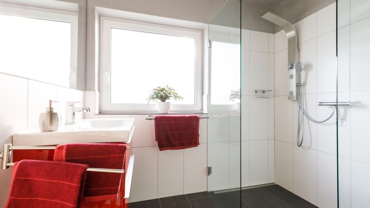 A modern bathroom with a glass shower and bright tiles. Red towels and a small plant add color to the space.