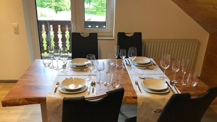 A beautifully set dining table with dishes and glasses. Through the window, one can see a green view.