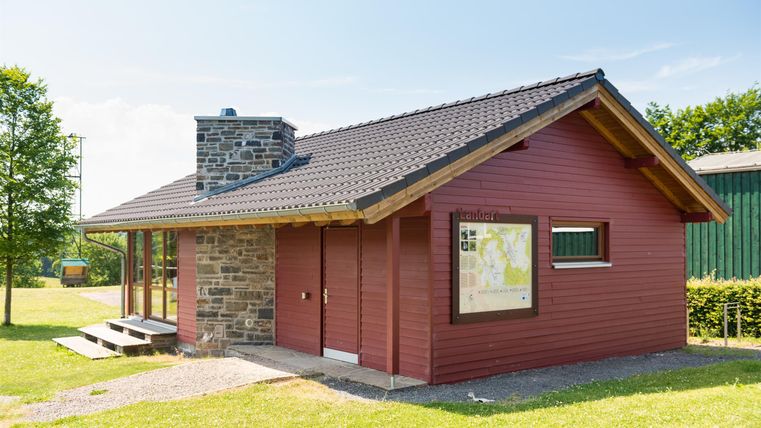 Een rood huis met een stenen voet en een schuin dak. Het ligt in een groene omgeving met een heldere lucht.