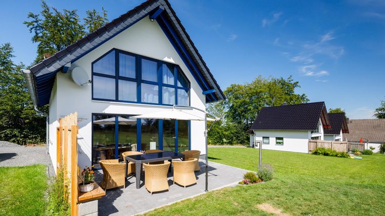 A modern house with large windows and a cozy outdoor area. The garden is green and inviting, perfect for relaxing.