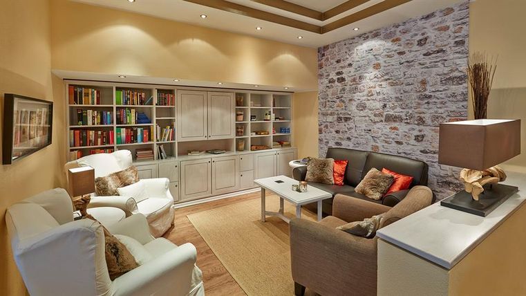 Ein gemütlicher Wohnzimmer mit bequemen Sesseln und einem modernen Bücherregal. Die Wände sind in warmen Farbtönen gehalten und schaffen eine einladende Atmosphäre.
