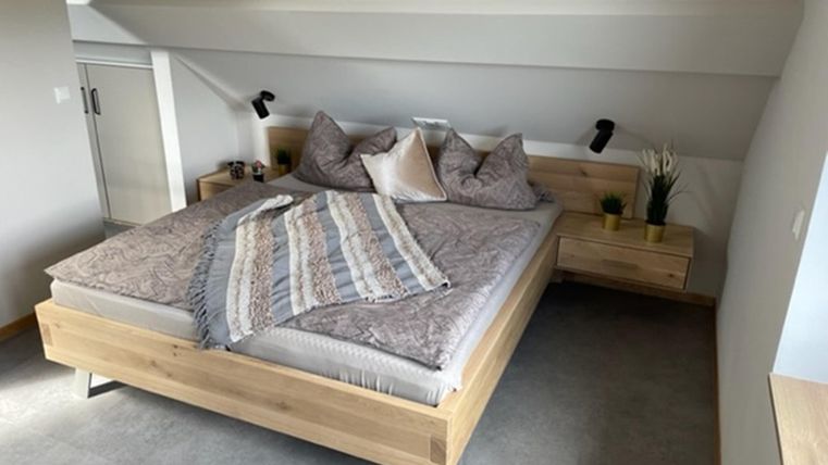 Een moderne slaapkamer met een groot houten bed en gezellige kussens. De muren zijn licht geschilderd en de vloer is met tapijt bekleed.