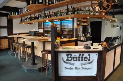 A modern restaurant with a wooden bar and a large selection of drinks. The decor is cozy and inviting.