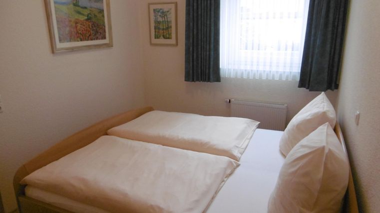 A cozy bedroom with a double bed and two single pillows. The window lets in a lot of daylight and is decorated with light curtains.