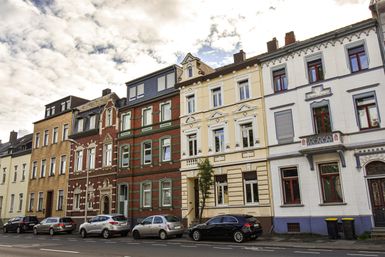 Eine Straße mit historischen Gebäuden in verschiedenen Farben. Parkende Autos ergänzen das Stadtbild.