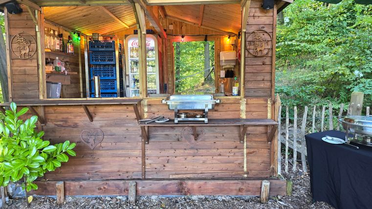 A wooden stand with windows and lighting in a green environment. On the table is a buffet with various foods.