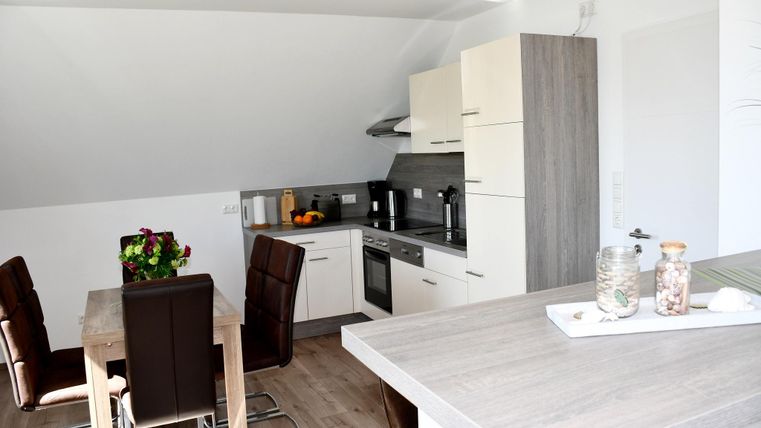 Een moderne keuken met een eettafel en gezellige stoelen. Helle kleuren en veel daglicht zorgen voor een uitnodigende sfeer.