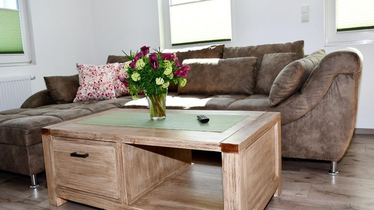 Een gezellige woonkamer met een bruin bank en een houten tafel. Op de tafel staat een boeket bloemen in een vaas.