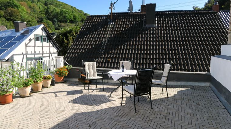 Een lichte terras met een tafel en stoelen. Omringd door planten en een prachtig uitzicht op de omliggende heuvels.