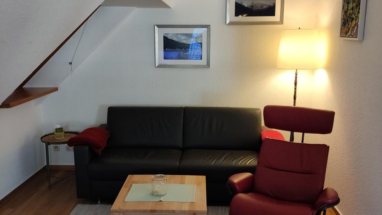 A cozy living room with a black sofa and a red armchair. The room is bright and inviting, with pictures on the wall and a floor lamp.