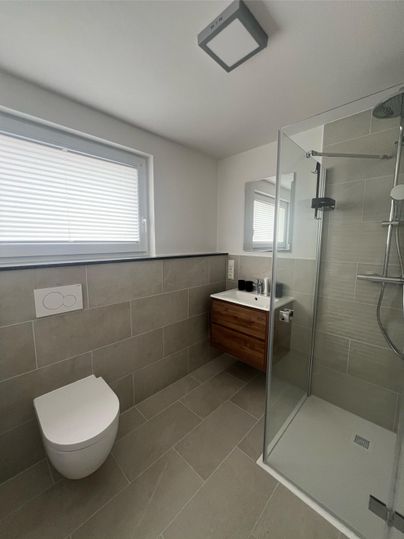 A modern bathroom with a glass shower and a stylish sink. The walls are in neutral colors, and there is a window for daylight.
