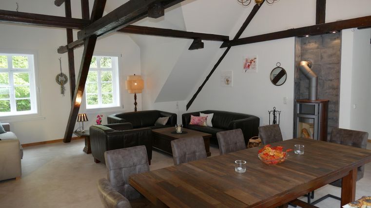 Een moderne woonkamer met houten balken en een gezellige zithoek. Een grote tafel nodigt uit tot eten en samenzijn.