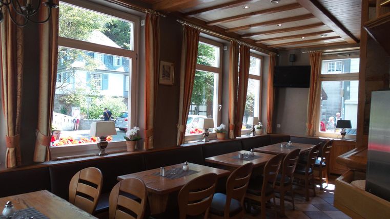 Een uitnodigend restaurant met houten tafels en stoelen. Grote ramen zorgen voor veel natuurlijk licht en een uitzicht naar buiten.