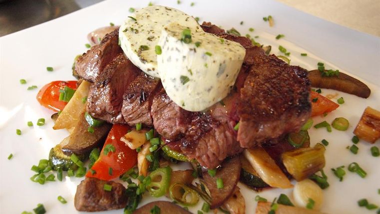 Een sappig stuk rundvleessteak op een bed van groenten. Daarbovenop is een stuk kruidenboter geserveerd.