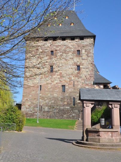 Ein historischer Turm aus Stein in einer grünen Umgebung. Der Himmel ist klar und blau.