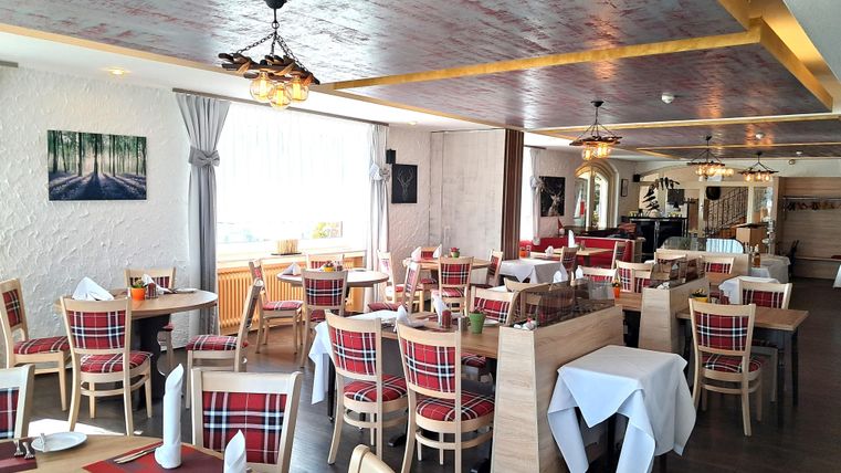 An elegant restaurant setting with tablecloths and set tables. In the foreground, there is a striking wine bottle rack.