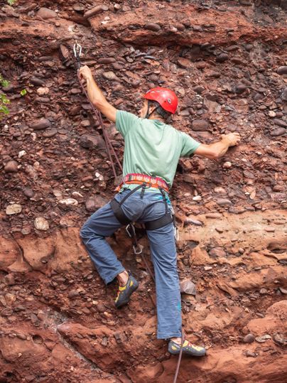 A climber with a helmet ascends a rock face. He is wearing climbing gear and focusing on the next hold.