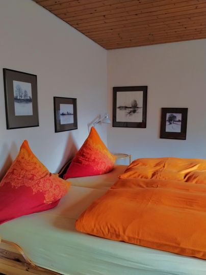 Een gezellige slaapkamer met een groot bed en feloranje kussens. De muren zijn versierd met verschillende ingelijste foto's.