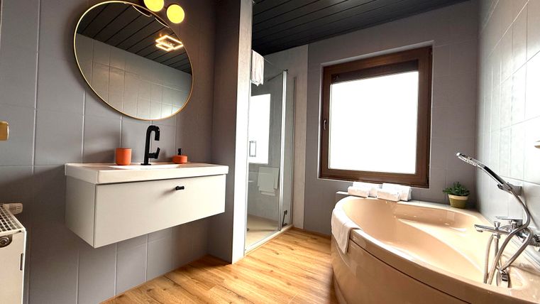 Een moderne badkamer met een ronde spiegel en een vrijstaande badkuip. De muren zijn in zachte kleuren geschilderd en de vloer is van hout.
