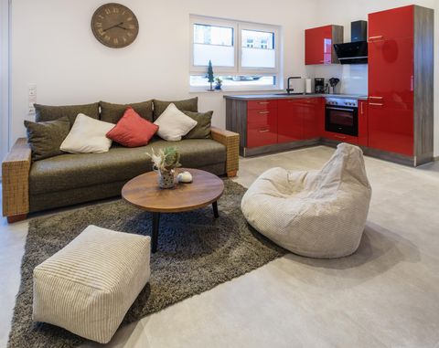 Een moderne woonkeuken met een gezellige bank en een ronde tafel. De rode keukenkasten zorgen voor een mooie accent in de ruimte.